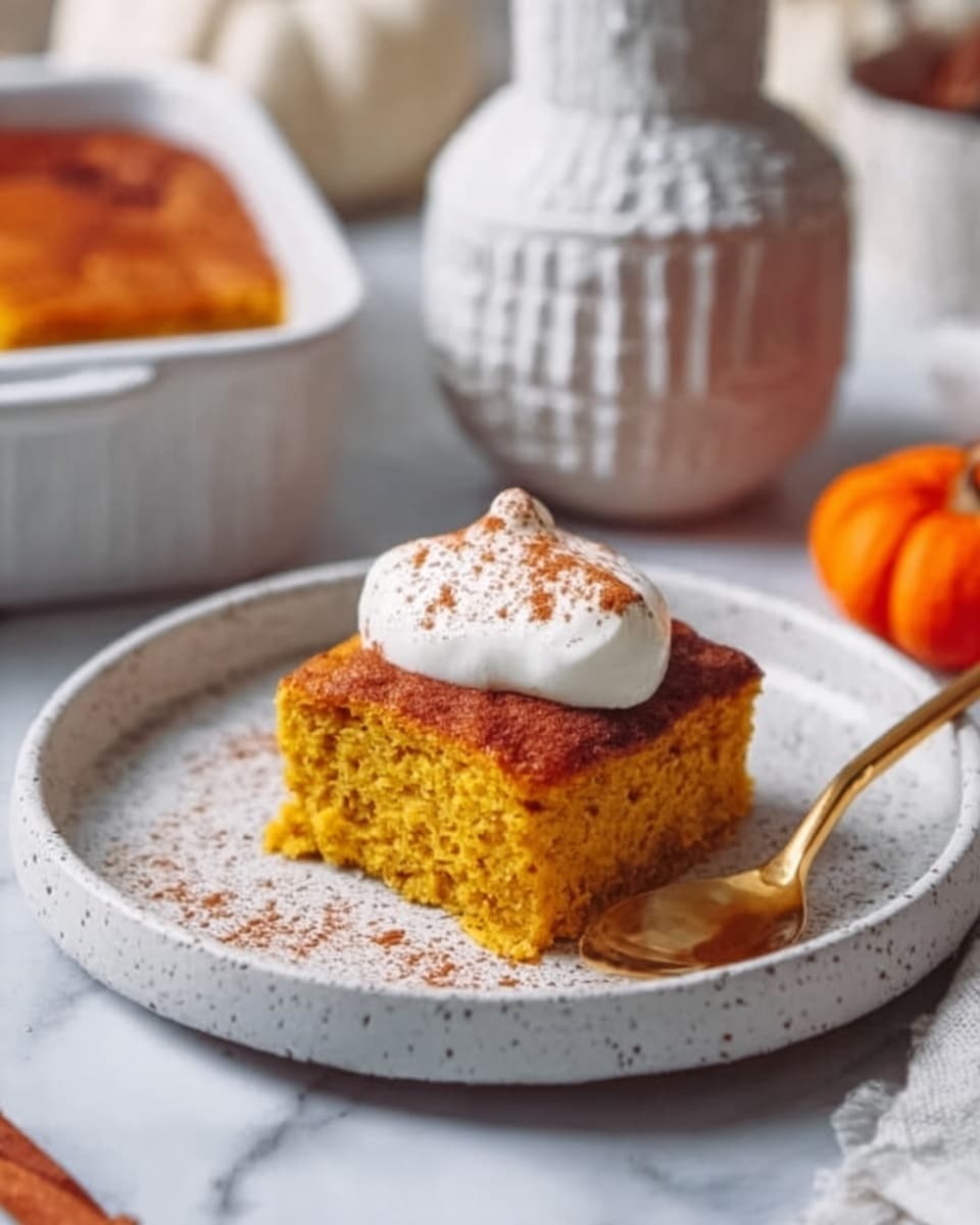 A piece of thick, golden-yellow cornbread sits in the middle of a white plate with a speckled pattern. On top of the cornbread is a large dollop of creamy white whipped topping, sprinkled lightly with cinnamon or nutmeg. The cornbread looks soft and moist, with a slightly crumbly texture on the sides. Next to the plate is a small white ceramic bowl and a wooden spoon, resting on a white marbled surface. The background includes a hint of pumpkin-orange color and a rustic wooden board. Photo taken with an iphone --ar 4:5 --v 7