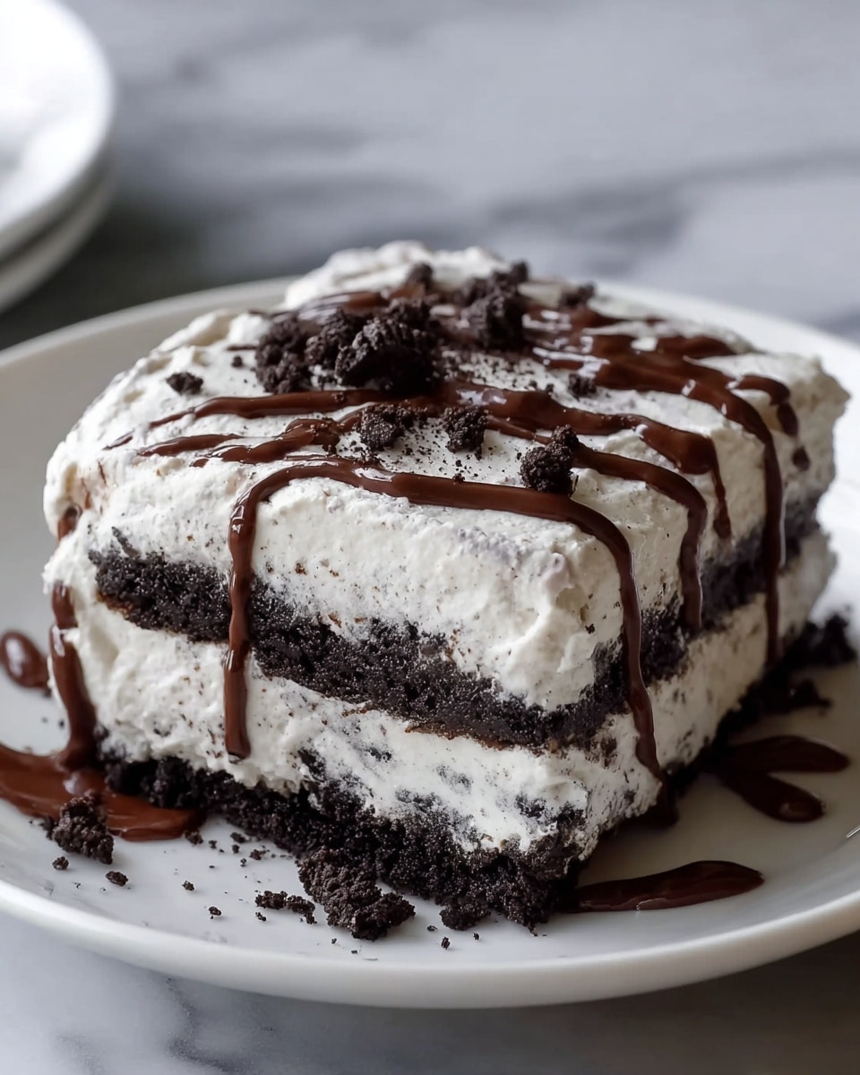 The image shows a close-up of a three-layer square dessert placed on a white plate with a glossy finish. The bottom layer is a dark, crumbly chocolate crust, followed by a thick, creamy white layer with dark specks throughout, suggesting cookies and cream filling. Above this is another thin dark chocolate layer, then topped with a thick, fluffy white cream layer, also speckled with dark bits. On the top, there are drizzles of dark chocolate sauce running vertically, along with small crumbles of chocolate cookies. The plate sits on a surface with a white marbled texture, and the background is softly blurred. photo taken with an iphone --ar 4:5 --v 7