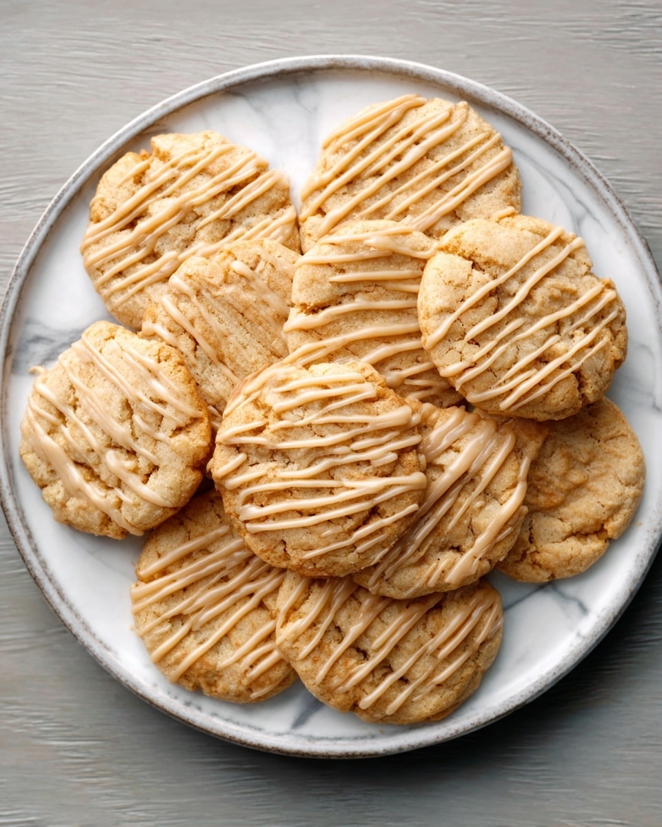 A white plate holds eight peanut butter cookies arranged in a circle. Each cookie is golden brown and has a slightly cracked surface with a crisscross pattern on top. A light drizzle of white icing is spread unevenly over each cookie, adding texture and contrast. The plate is placed on a white marbled textured surface. Photo taken with an iphone --ar 4:5 --v 7