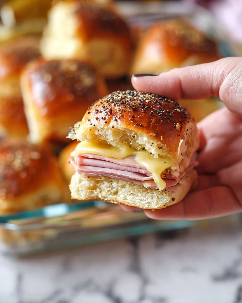 A close-up of a small sandwich held by a woman's hand showing three layers: the top layer is a shiny golden-brown bread bun sprinkled with black poppy seeds, the middle layer is a pale yellow melted cheese, and the bottom layer is a slice of pink ham. The sandwich is soft and slightly glossy. In the background, several similar sandwiches are in a clear glass dish on a white marbled surface. Photo taken with an iphone --ar 4:5 --v 7