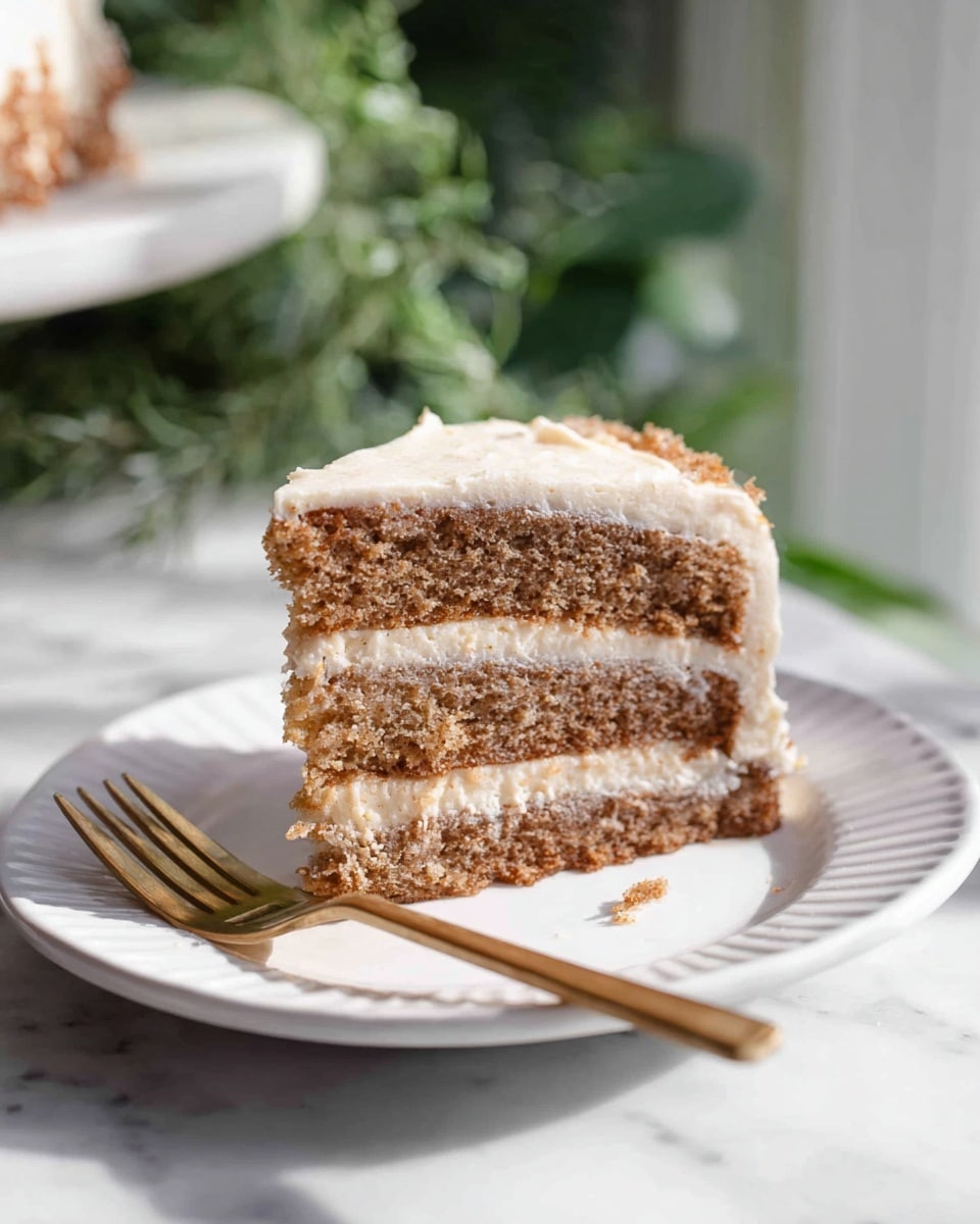 A slice of three-layer brown cake with light cream-colored frosting between each layer and on the outside edges sits on a white plate. The cake layers look moist and soft with a slightly crumbly texture. The frosting is creamy and spread evenly but not perfectly smooth, giving a homemade feel. A golden colored fork is placed to the left of the cake on the plate. The plate is set on a white marbled surface, with soft natural light coming from the left side. Green blurred foliage is in the background behind the plate. Photo taken with an iphone --ar 4:5 --v 7