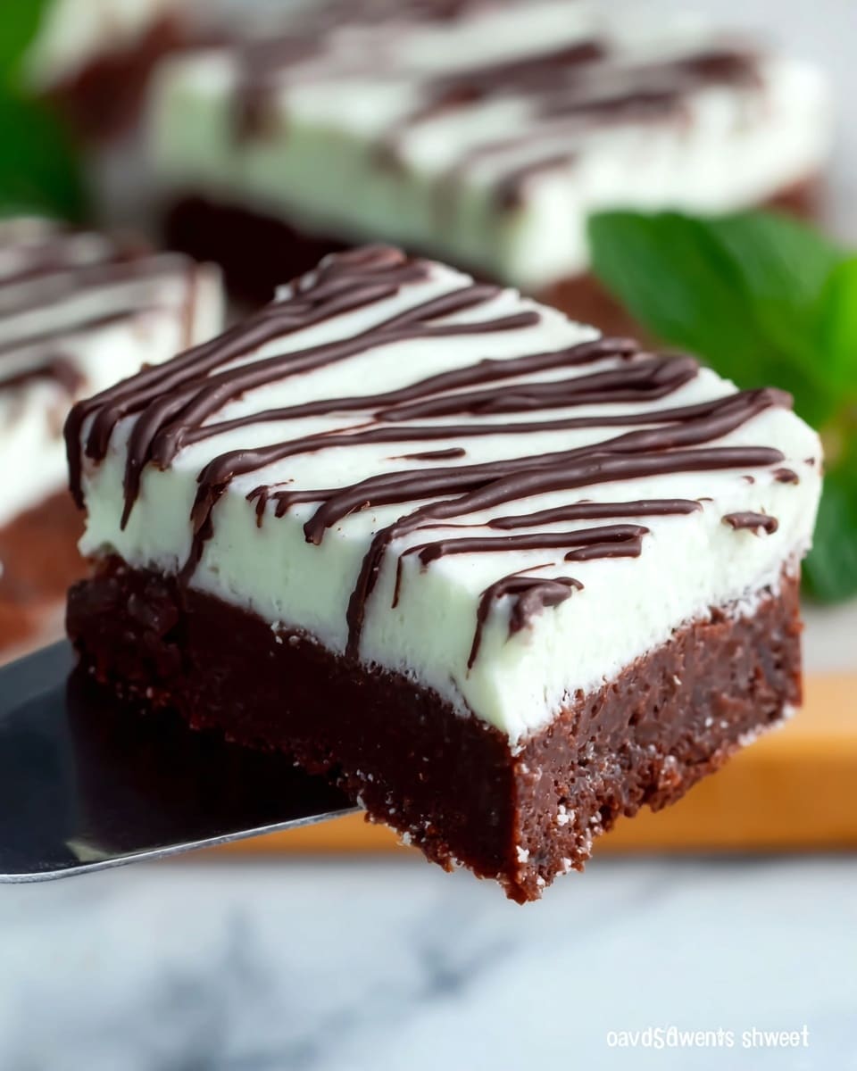A stack of three square dessert bars is shown on a white marbled surface, each bar having three visible layers: a thick, dense dark brown chocolate brownie base, a thick light green creamy mint layer with a smooth texture, and a topping of thin dark chocolate drizzle in lines on the green layer. The top bar has a bite taken out of its corner, revealing the soft texture of the mint layer and brownie beneath, and is decorated with a small fresh green mint leaf on top. Photo taken with an iphone --ar 4:5 --v 7