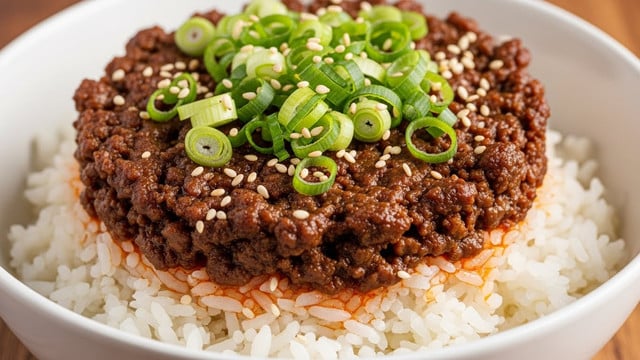 A close-up image of a white bowl filled with a layered dish, starting with a bottom layer of soft, fluffy white rice. On top, there is a thick layer of dark brown cooked ground meat with a slightly oily texture, giving it a shiny look. The meat is garnished with thinly sliced, bright green scallions scattered evenly across the top, and small white sesame seeds are sprinkled over everything. Light reddish oil pools slightly around the edges where the meat meets the rice, adding a rich contrast. The bowl sits on a wooden surface with a warm tone, and the photo is sharp and bright, highlighting the textures clearly. Photo taken with an iphone --ar 4:5 --v 7